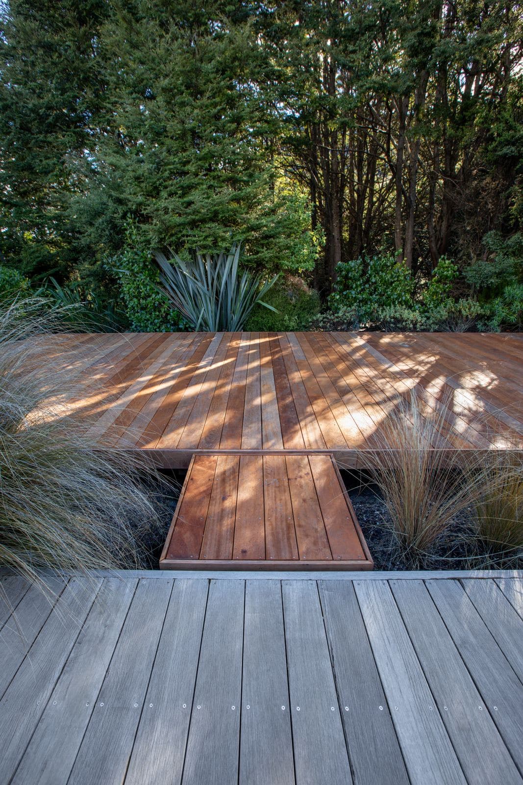 A short timber bridge crossing tussock between two decks, trees behind