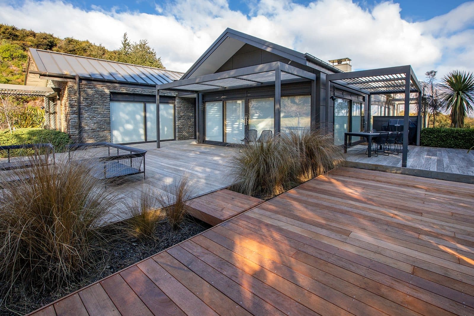 Hardwood decks stepping between tussock planting and a stone house with pergolas