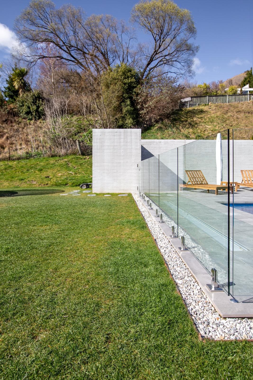 A glass pool fence on a gravel strip, steel edging keeping the lawn line