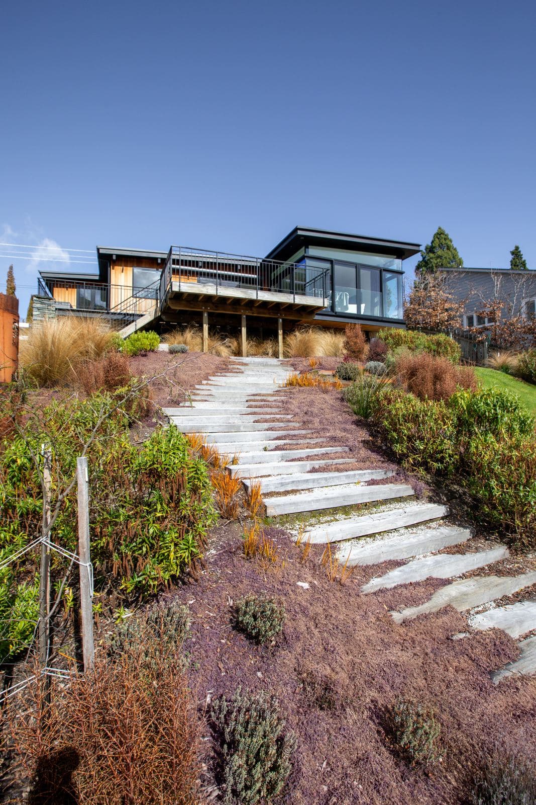 Stone slab steps running up a planted bank to a house under blue sky
