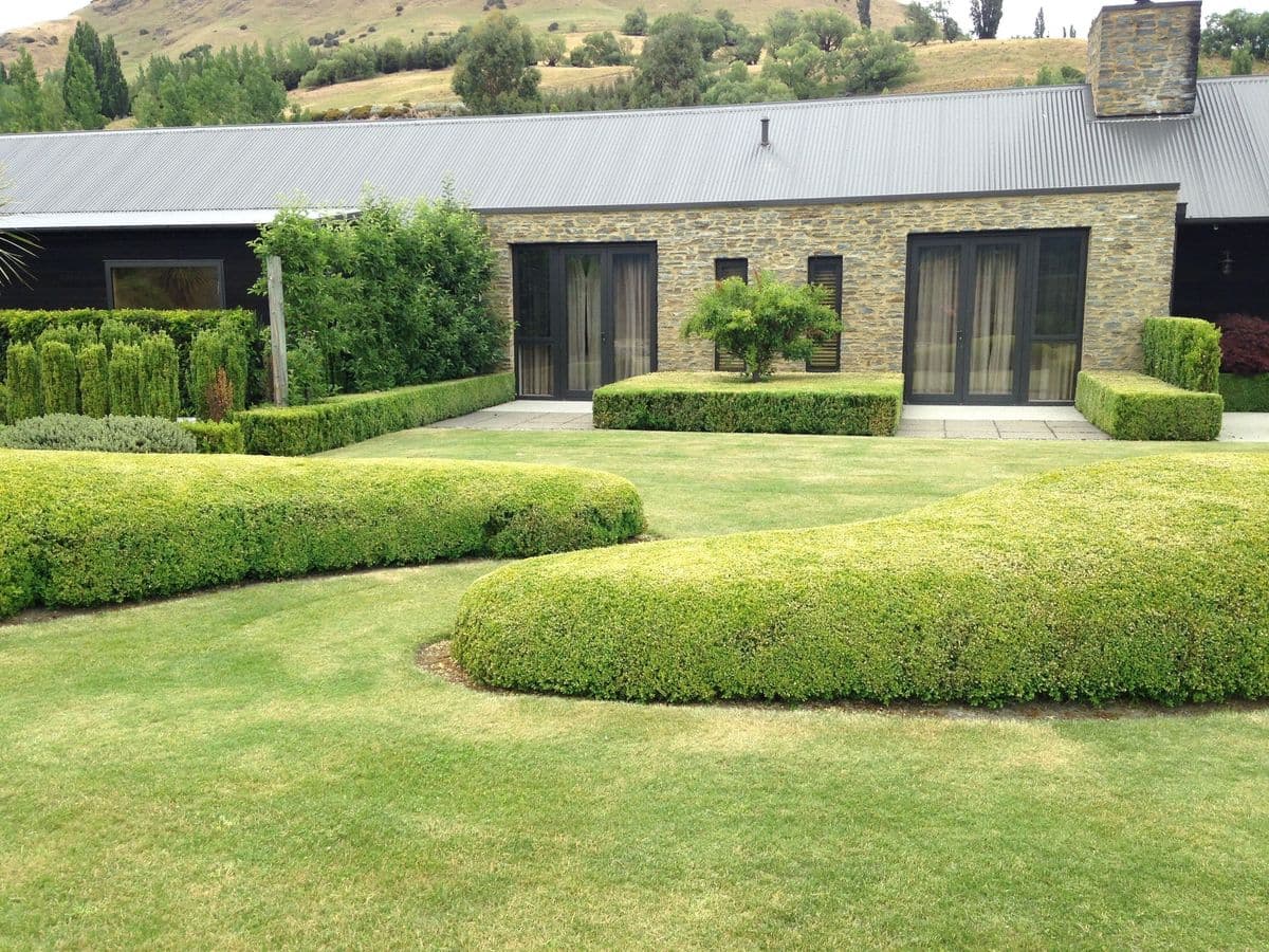 A clipped, formal Diva garden beside a stone home in the Whakatipu
